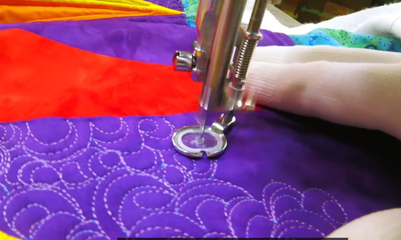 A sewing machine doing a dense, swirly free-motion quilting design on a purple fabric to create background texture on a quilt.