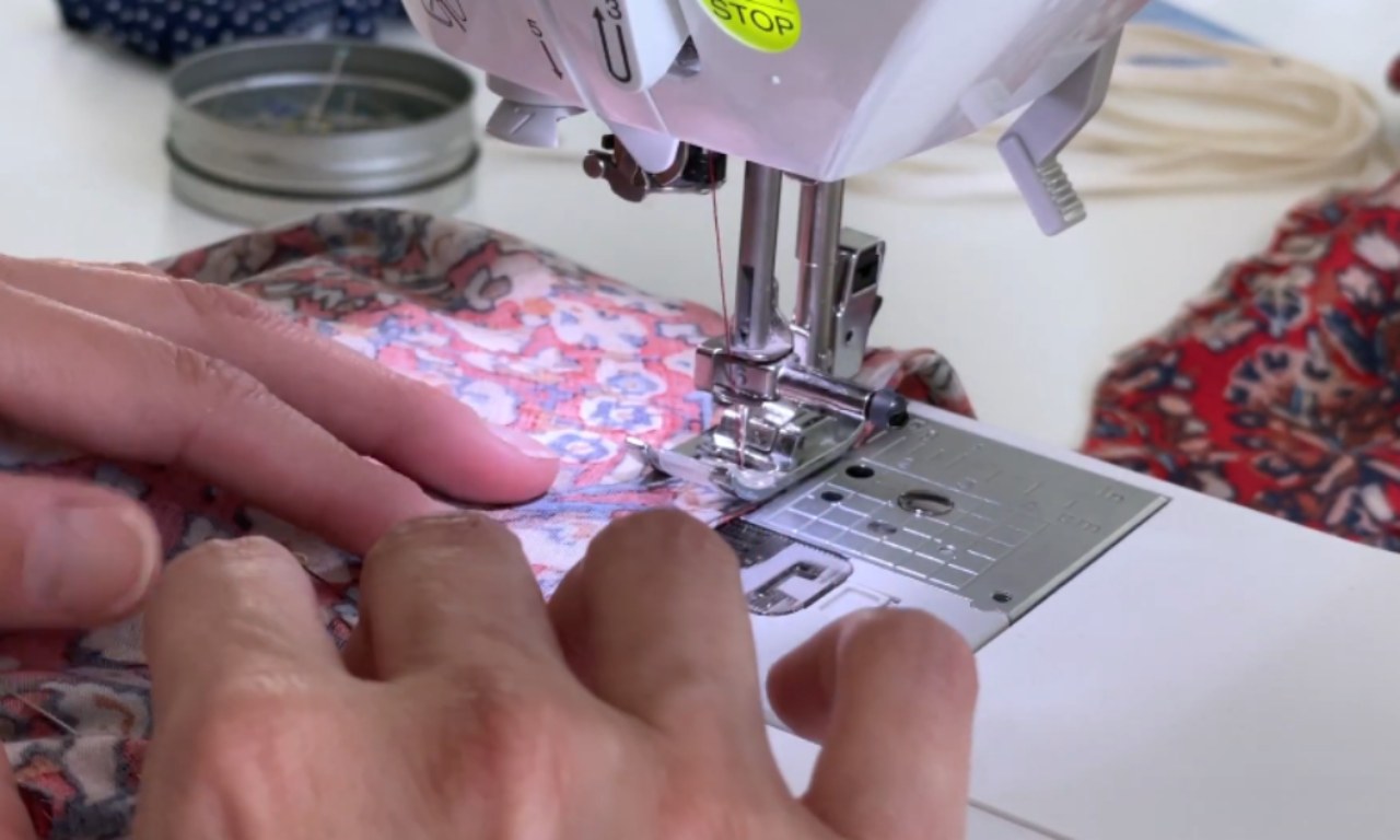 Close-up of hands sewing a patterned fabric on a sewing machine to create a seam for a peasant blouse.