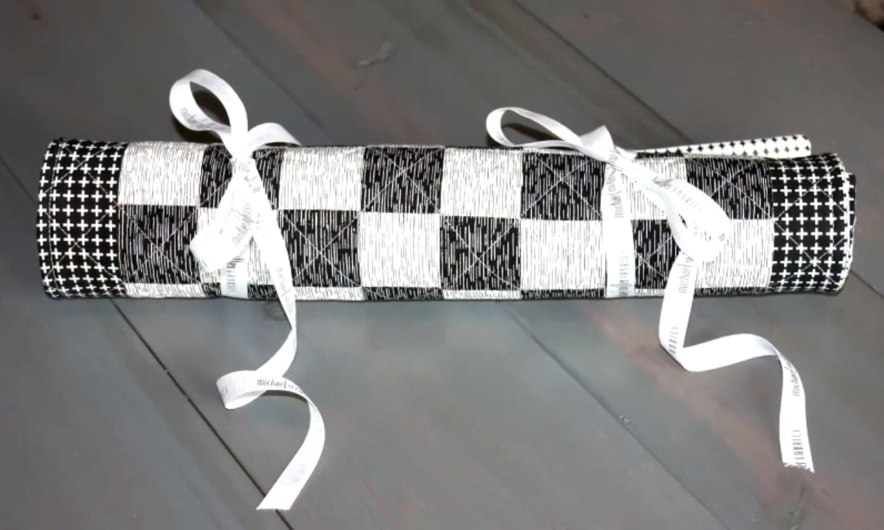 A rolled-up quilted checkerboard tied securely with white ribbon, designed as a portable game board for easy travel and storage.