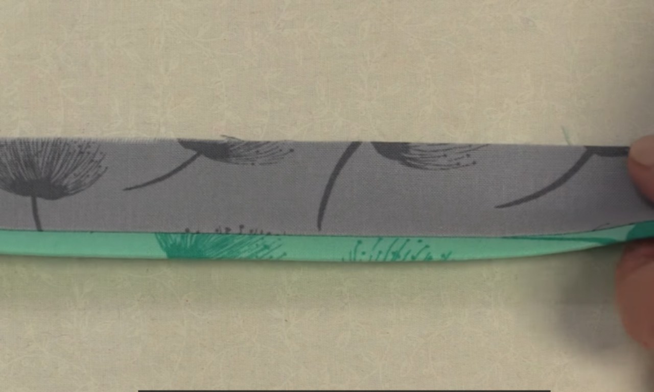 A close-up of the prepared faux flanged binding strip, showing the gray main binding fabric folded over the turquoise flange fabric before sewing it to the quilt.