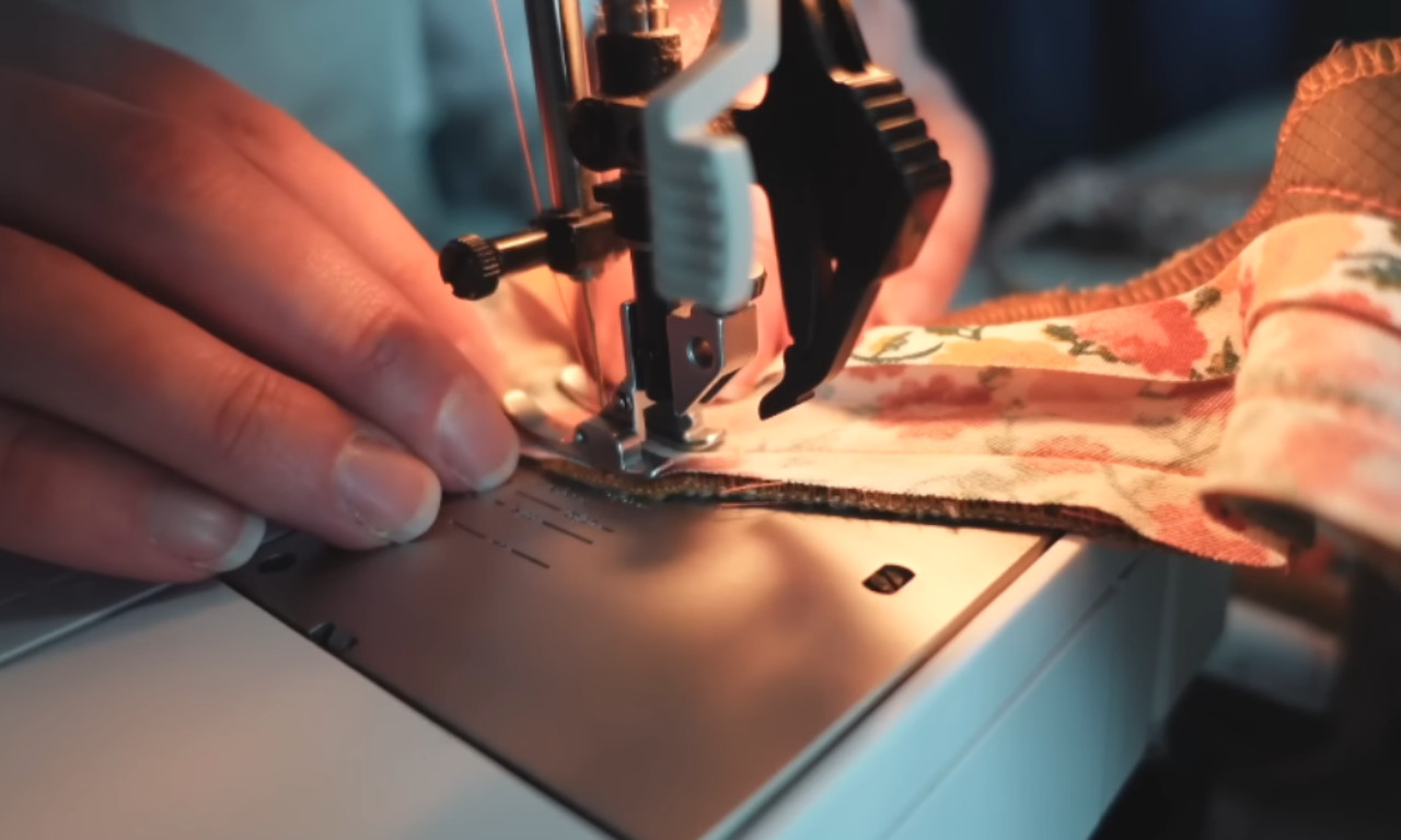 Close-up of a sewing machine stitching floral binding onto quilted fabric, with a person guiding the fabric by hand.