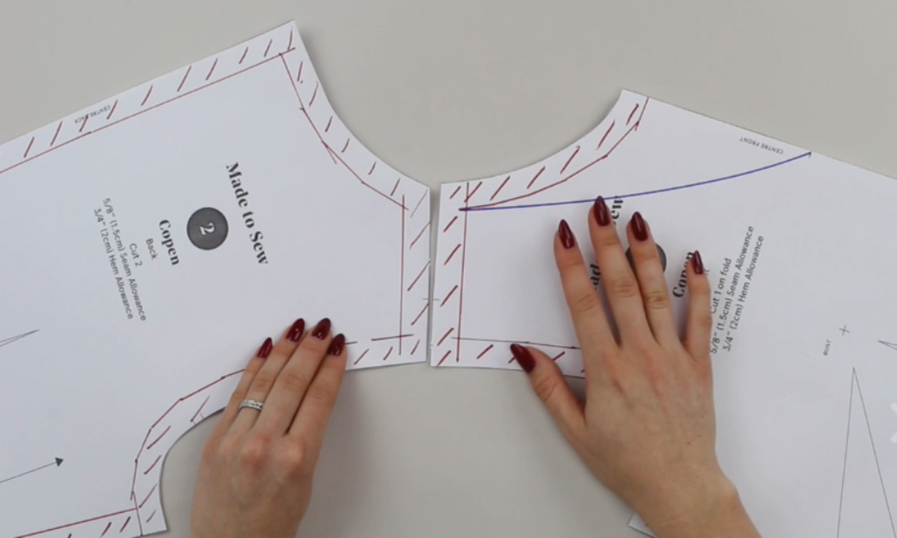 A person truing the seams of a bodice pattern by aligning the shoulders of the front and back pieces to ensure the newly drafted V-neckline fits correctly.