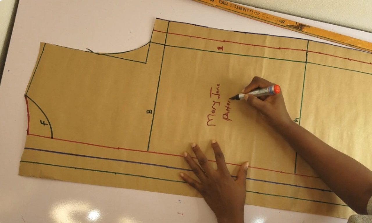 A hand holding a brown paper dressmaking pattern with lines and measurements drawn in different colors.
