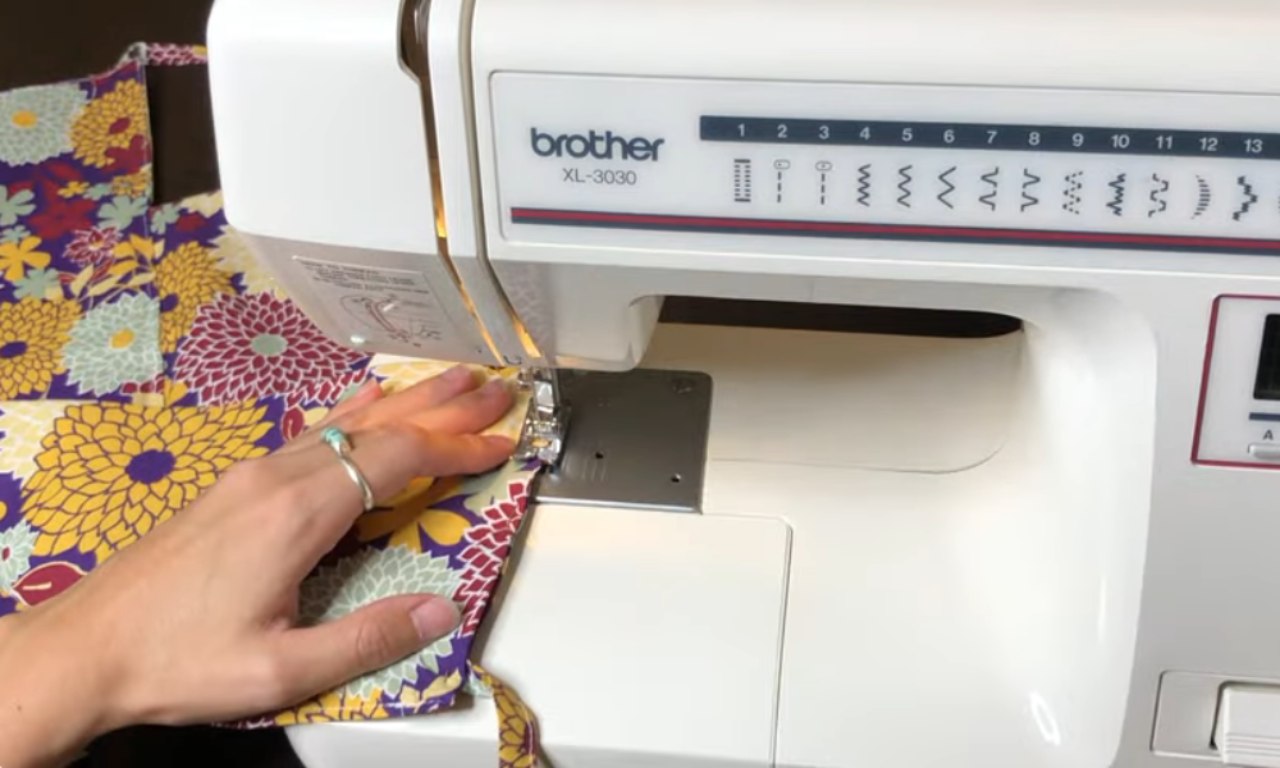 Close-up of a sewing machine stitching colorful floral fabric while a hand guides the material, working on tie straps for a halter top.