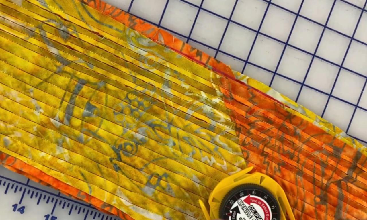 A yellow chenille cutter slicing through the top layers of flannel fabric between the sewn lines to create the fluffy texture for a DIY chenille scarf.