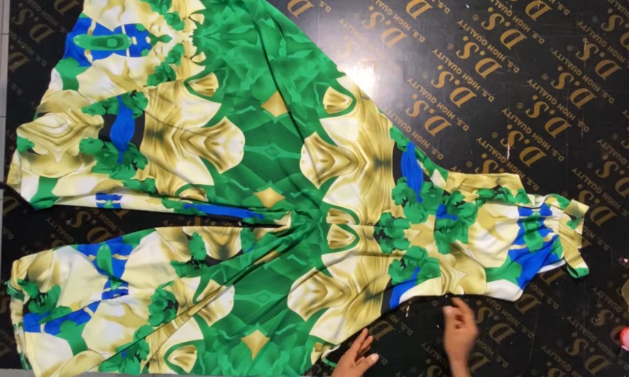 A brightly colored green, yellow, blue, and cream patterned fabric laid out flat on a black table, being prepared for sewing into a garment.