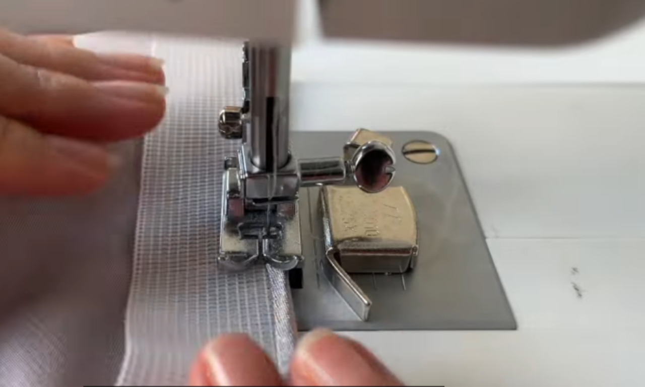 A close-up view of a sewing machine stitching a clean seam on the white interfaced facing for the DIY satin slip skirt.