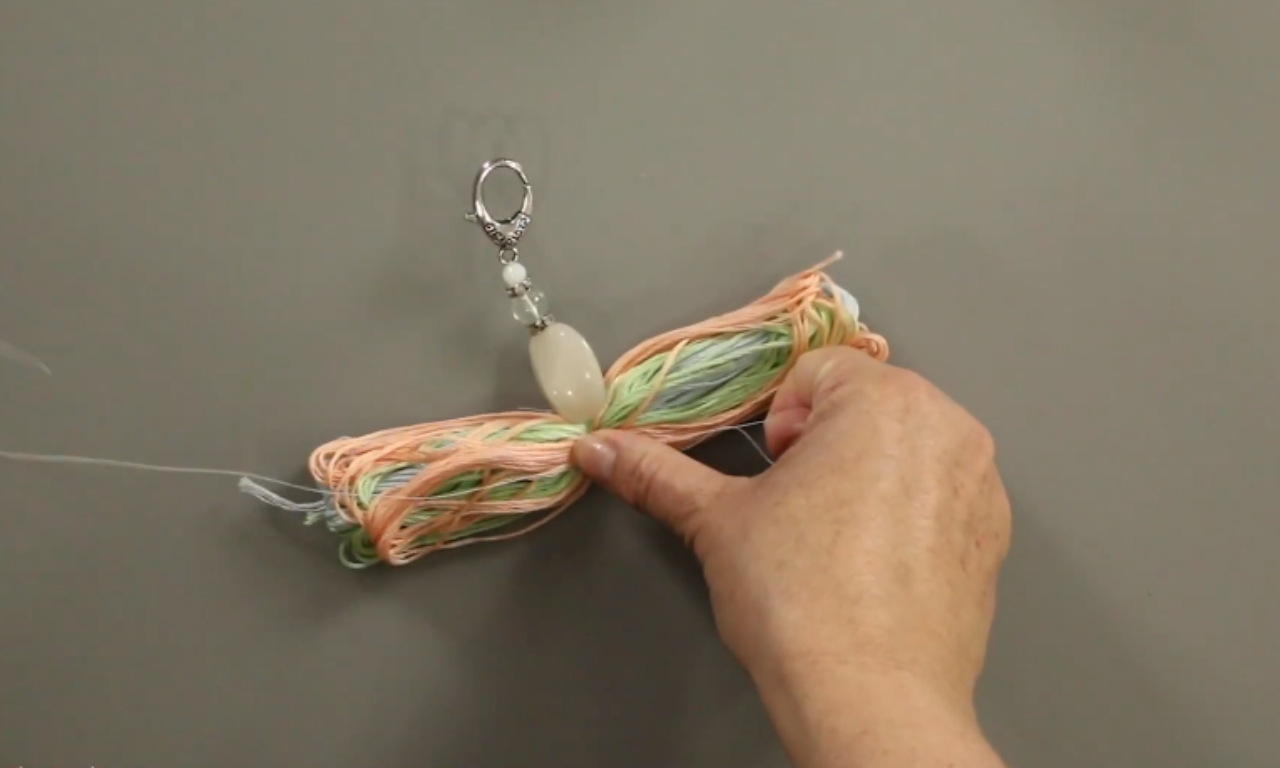 A step-by-step image showing how to make a tassel by tying a piece of yarn around the main body to create the tassel's neck.