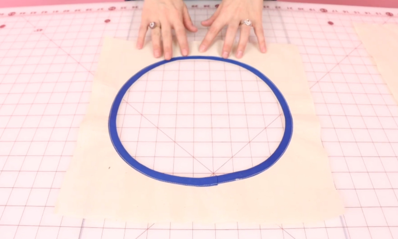 A step-by-step sewing process showing how to apply bias binding to a circular neckline. The first image shows a sewing machine stitching blue bias tape onto cream fabric with pins holding it in place. The second image shows hands folding and pinning the bias tape neatly around the neckline. The third image shows the completed neckline with the blue bias tape sewn smoothly in a circle on cream fabric.