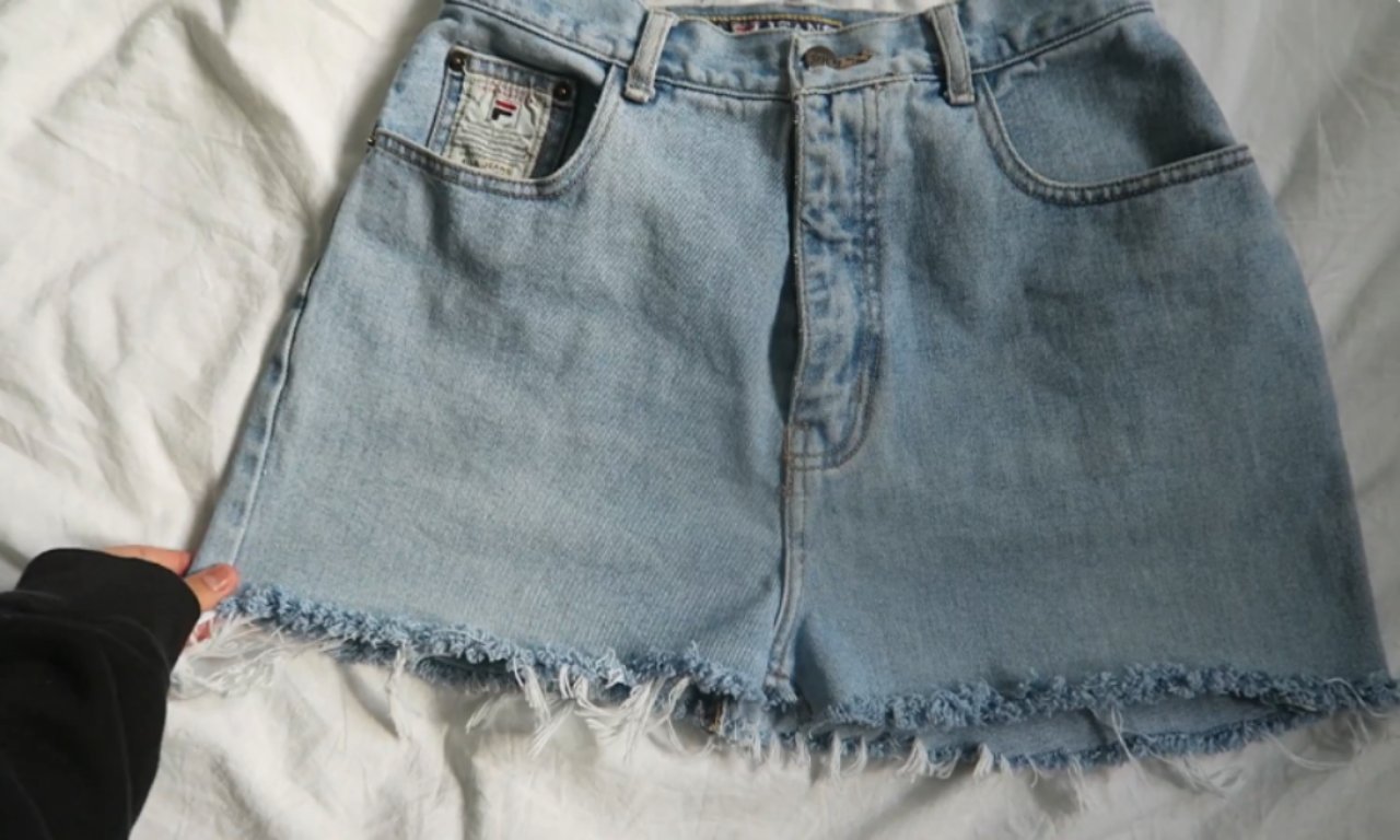 A finished light-wash DIY denim skirt made from old Fila jeans, laying flat on a white surface. The skirt has a frayed, raw hem, showing the successful result of the upcycling project.