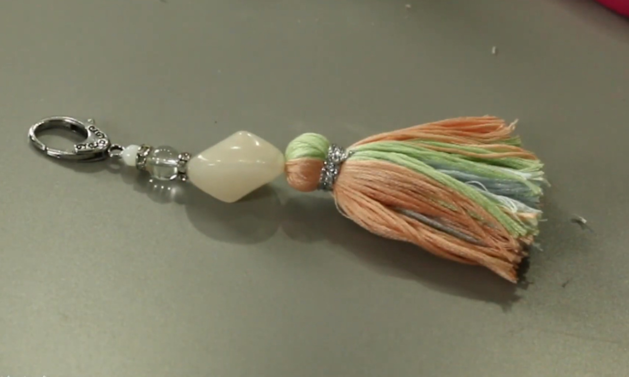 The finished DIY yarn tassel keychain, showing the neat tassel made from scrap yarn, decorative beads, and a silver clasp.