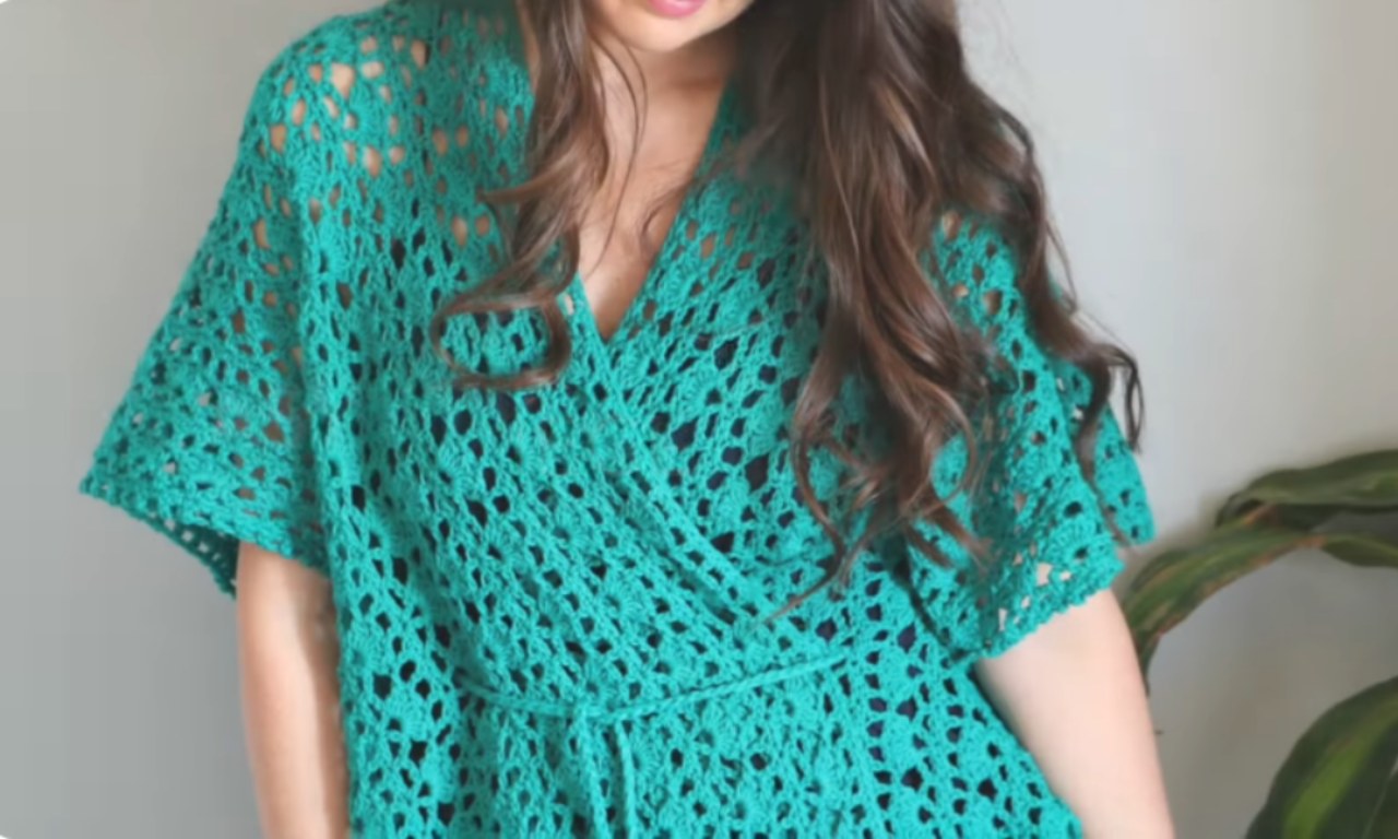 A woman models a finished teal green lacy crochet kimono cardigan with short, wide sleeves and an open-work stitch pattern.