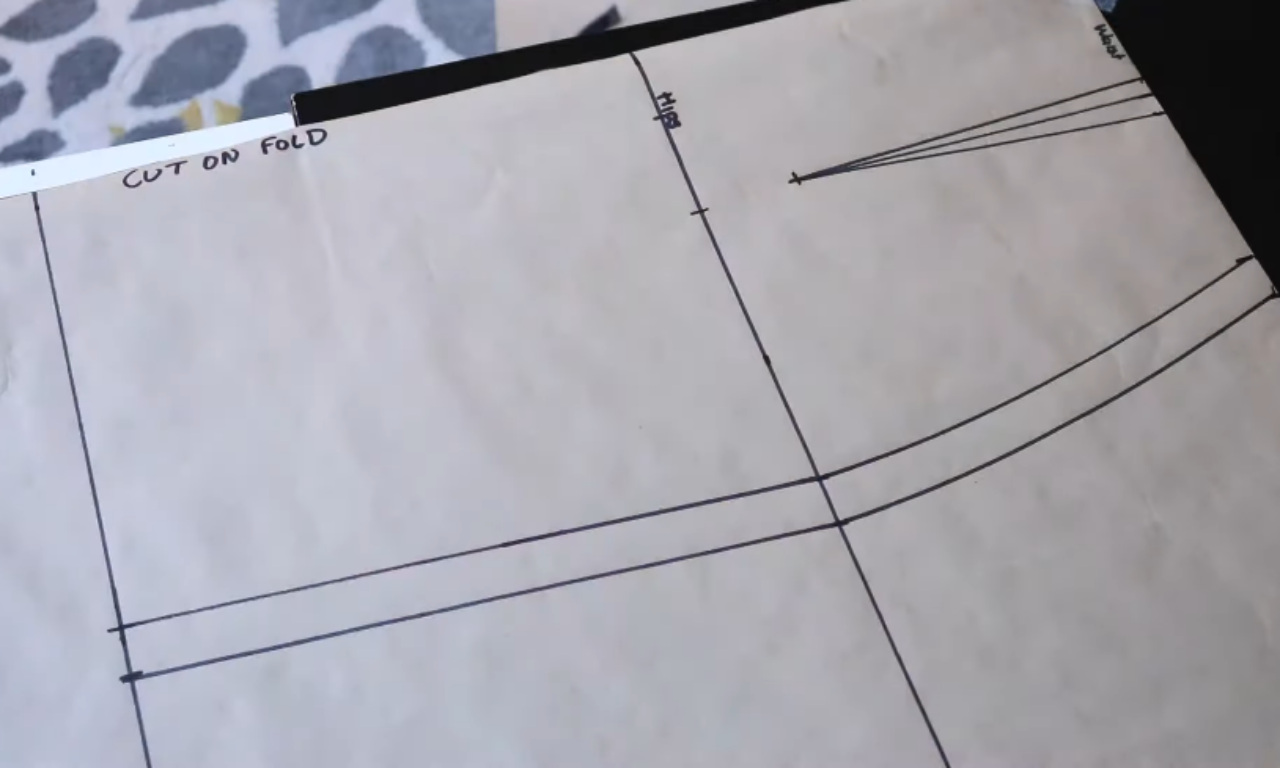 A close-up of a hand-drawn maxi skirt pattern on brown paper, showing the waist, hip curve, and dart lines with "CUT ON FOLD" written along the edge.