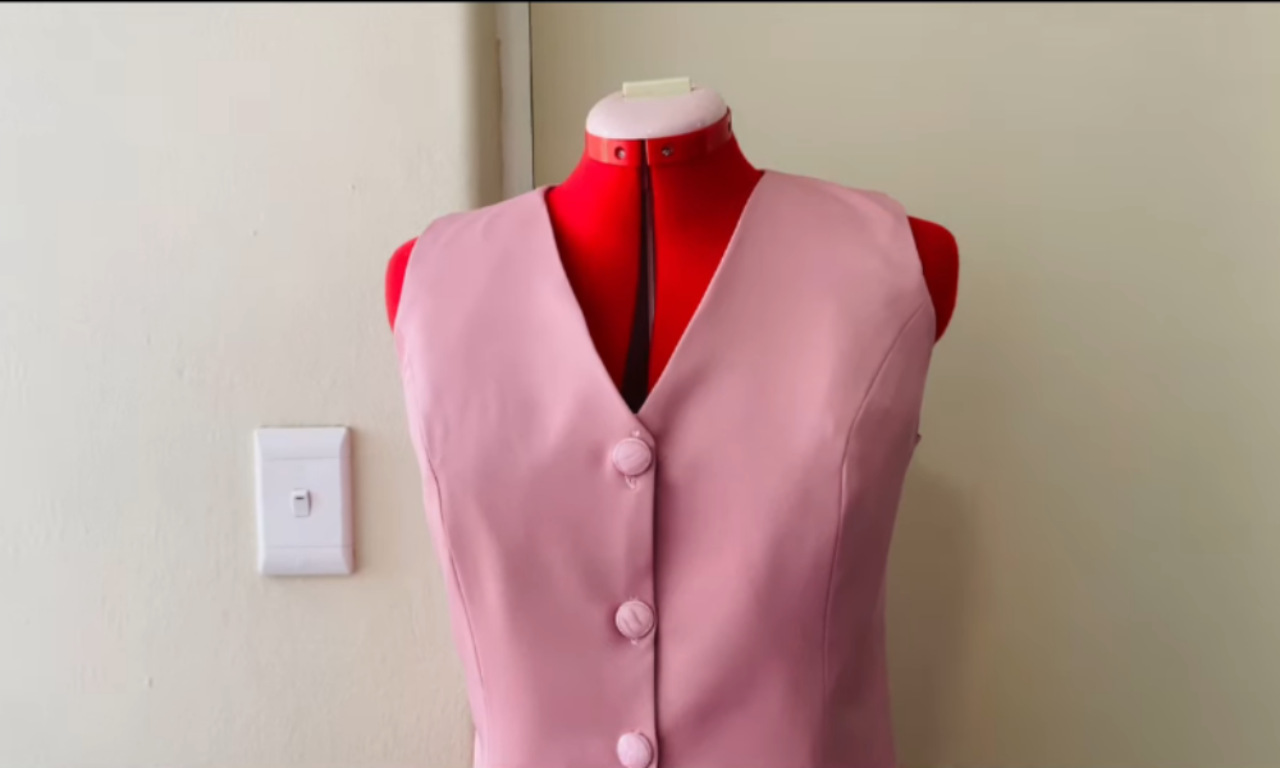 A finished light pink sleeveless vest with matching fabric-covered buttons displayed on a red dress form.