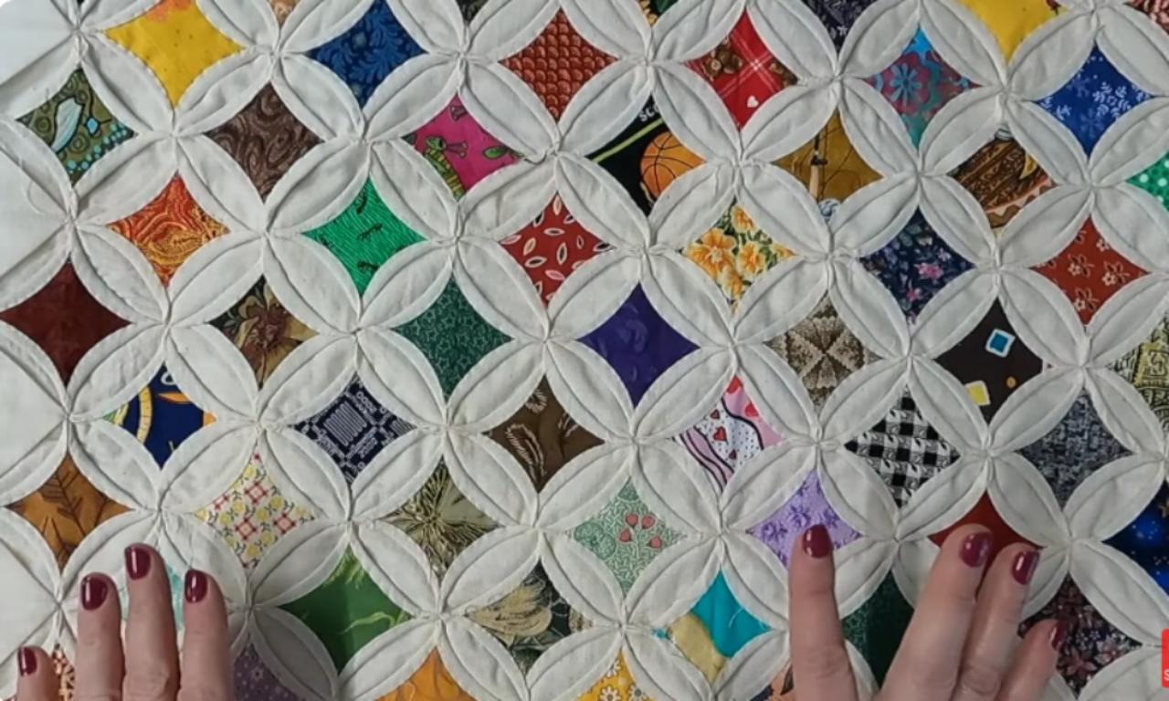 A close-up view of a finished Cathedral Window quilt, showing many colorful fabric scraps framed by folded cream-colored muslin to create a stained-glass effect.