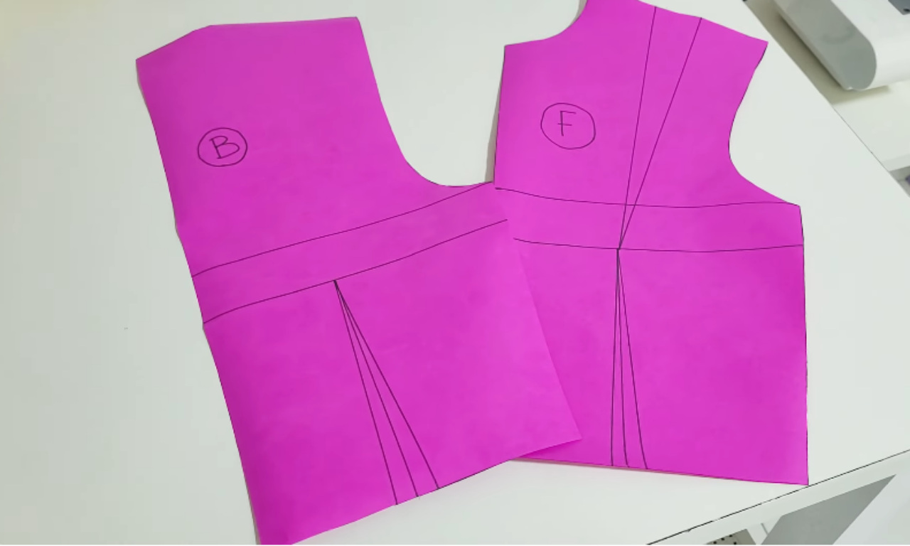 Two bright pink paper cutouts labeled "B" and "F," representing the back and front pieces of a crop top sewing pattern with marked darts and seams.