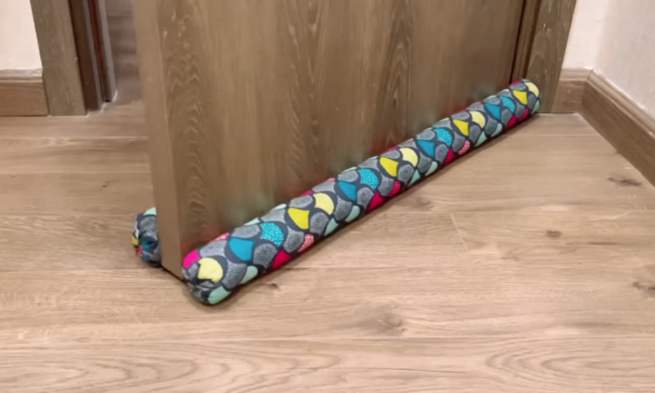 A colorful fabric draft stopper placed under a wooden door, sealing the gap at the bottom.