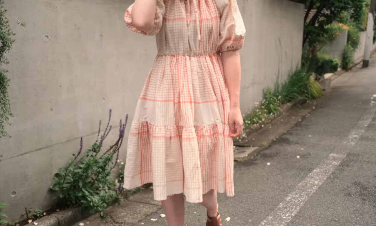 A woman models the finished gathered bodice romper, showcasing the puffy sleeves and tiered plaid skirt.