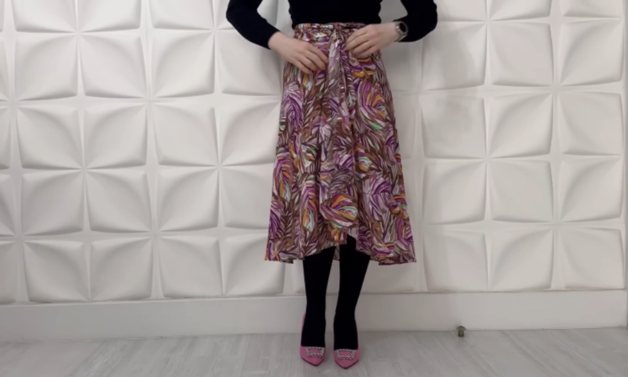 A person wearing a finished wrap skirt made from a vibrant, multicolored leaf-patterned fabric, tied at the waist, styled with black tights and pink heels.