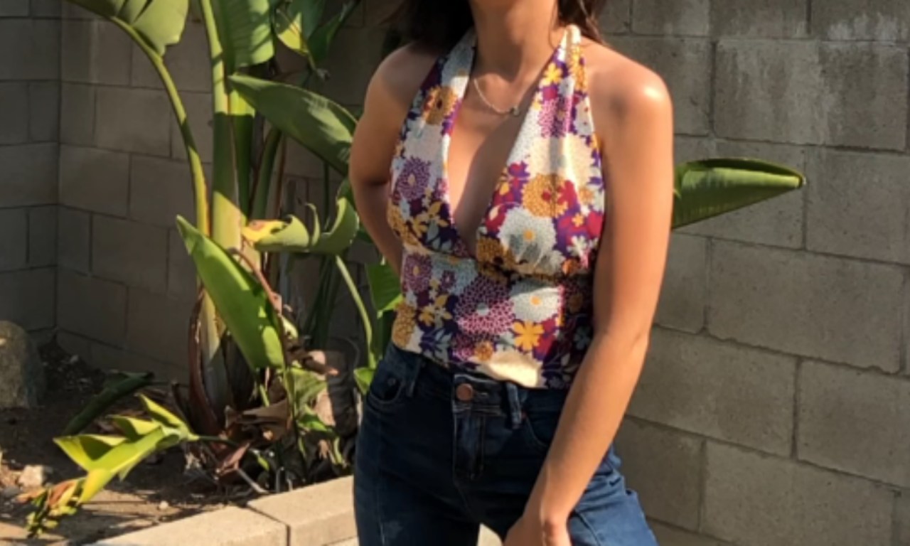 Person wearing a handmade floral halter top with a plunging neckline, paired with jeans, standing outdoors near a garden wall.