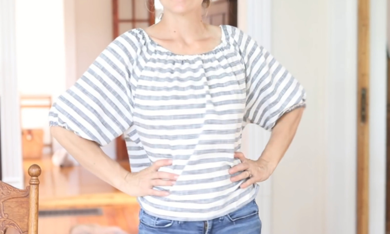 A woman wearing a finished grey and white striped peasant blouse with a gathered neckline and full sleeves.