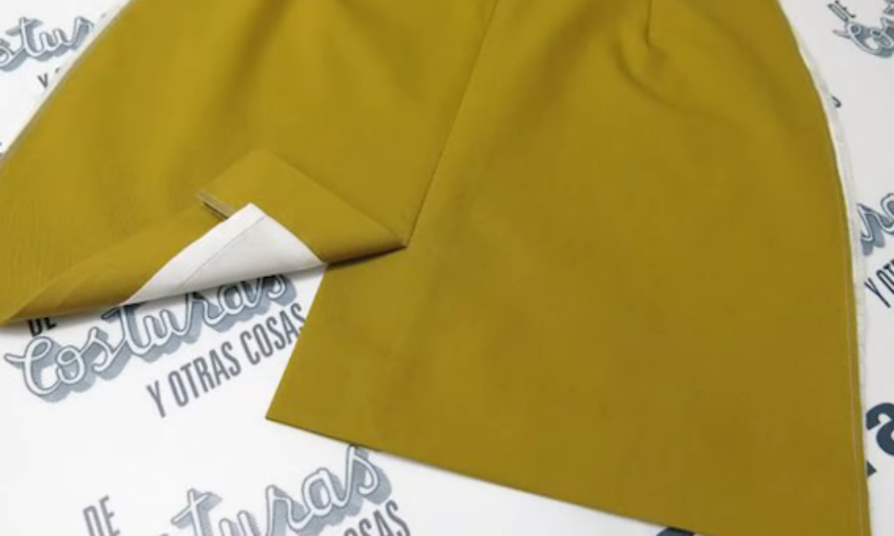 close-up of a finished skirt vent on a mustard-yellow skirt, with the corner folded back to show the white lining.