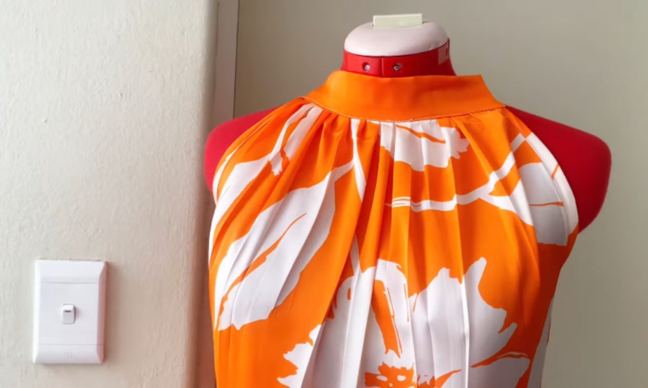 A close-up of a finished orange and white tiered halter dress on a red mannequin, showing the gathered fabric at the neckline.
