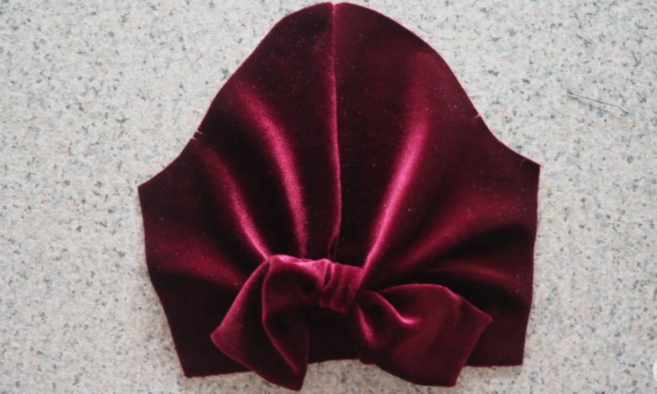 A burgundy velvet sleeve piece with gathered pleats and a bow detail in the center, displayed on a flat surface.