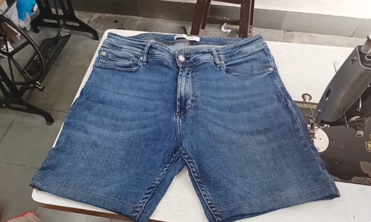A pair of blue denim jeans that have been successfully turned into shorts, lying on a table next to a sewing machine.