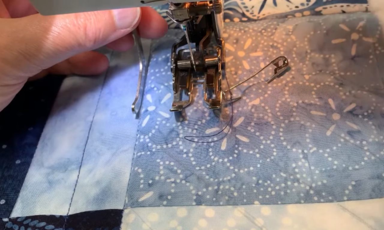 Person quilting on a sewing machine, wearing white grip gloves, guiding a layered quilt sandwich under the walking foot.