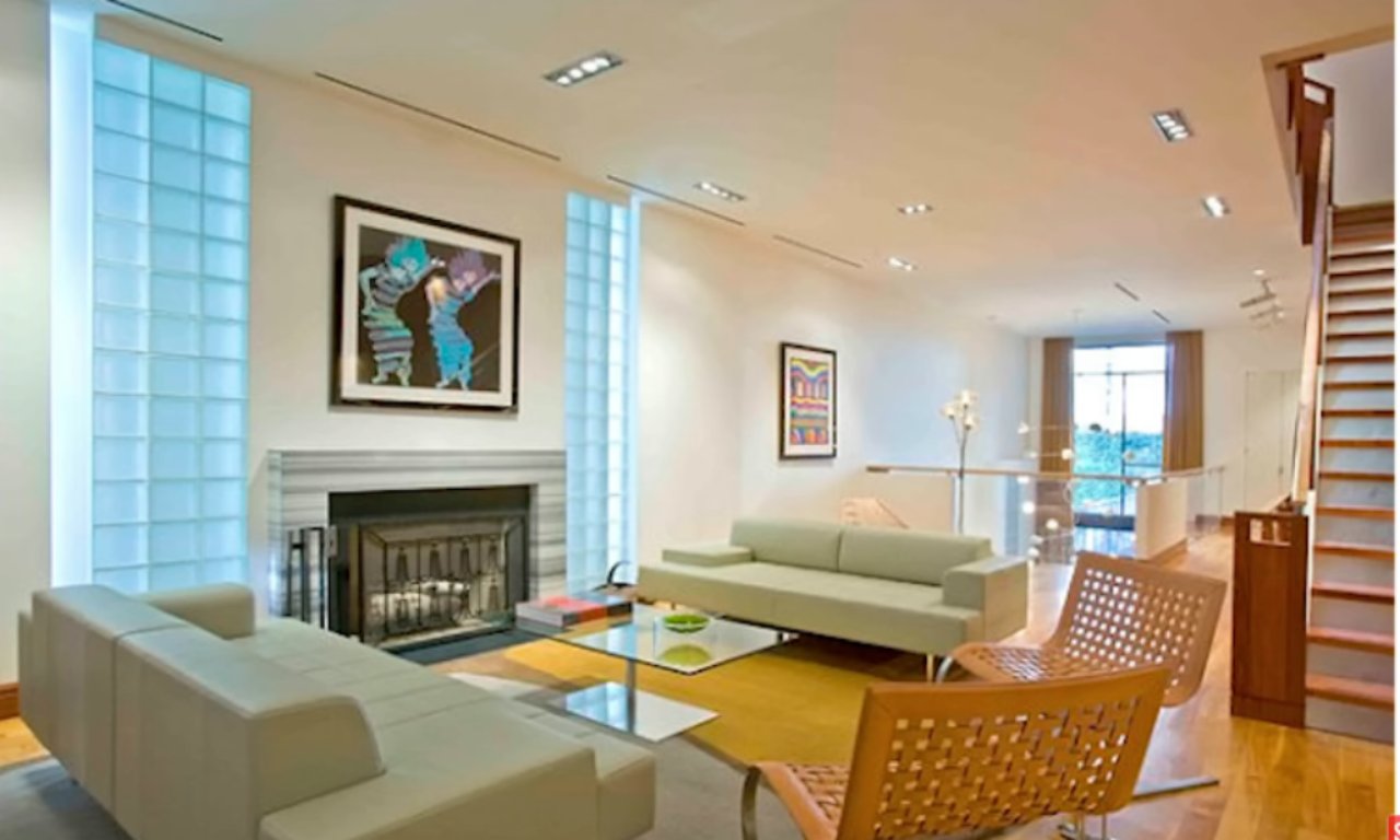 Modern living room with minimalist furniture, a fireplace, abstract artwork on the walls, and a wooden staircase leading upstairs.