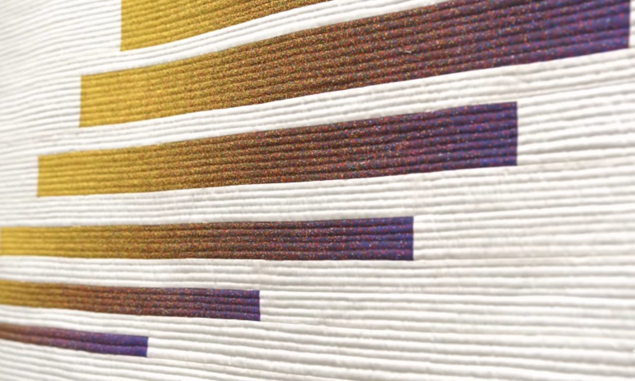 A minimalist quilt featuring horizontal bars in a gradient from yellow to purple, set against a white, heavily textured background with tightly spaced horizontal quilting lines.