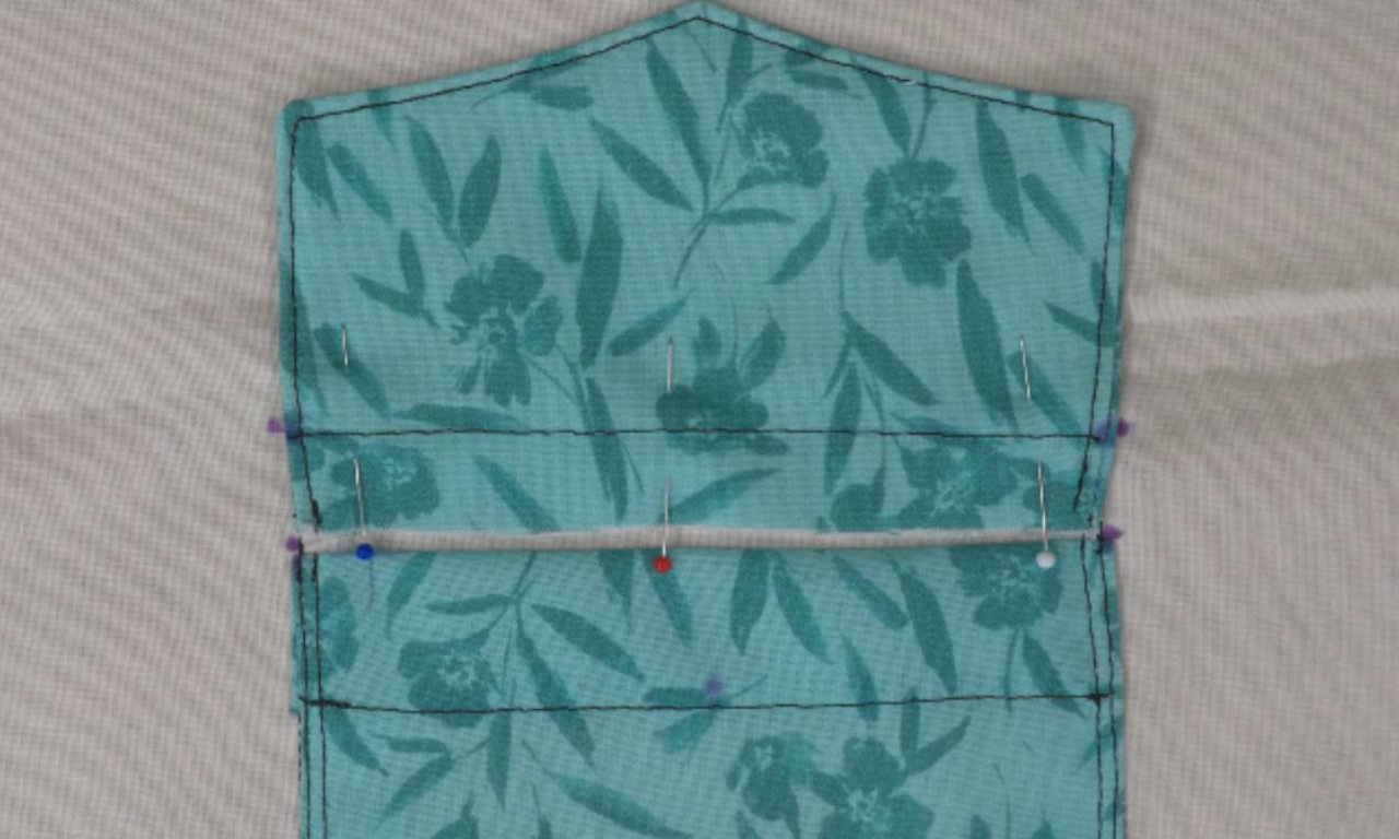 Pocket placement marked on fabric with pins securing a teal floral pocket piece onto a light base fabric