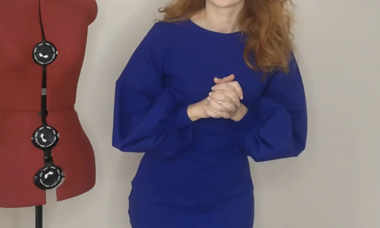 A woman is wearing a fitted blue dress with voluminous bishop sleeves gathered at the wrist with simple stretchy cuffs, showcasing the finished garment.