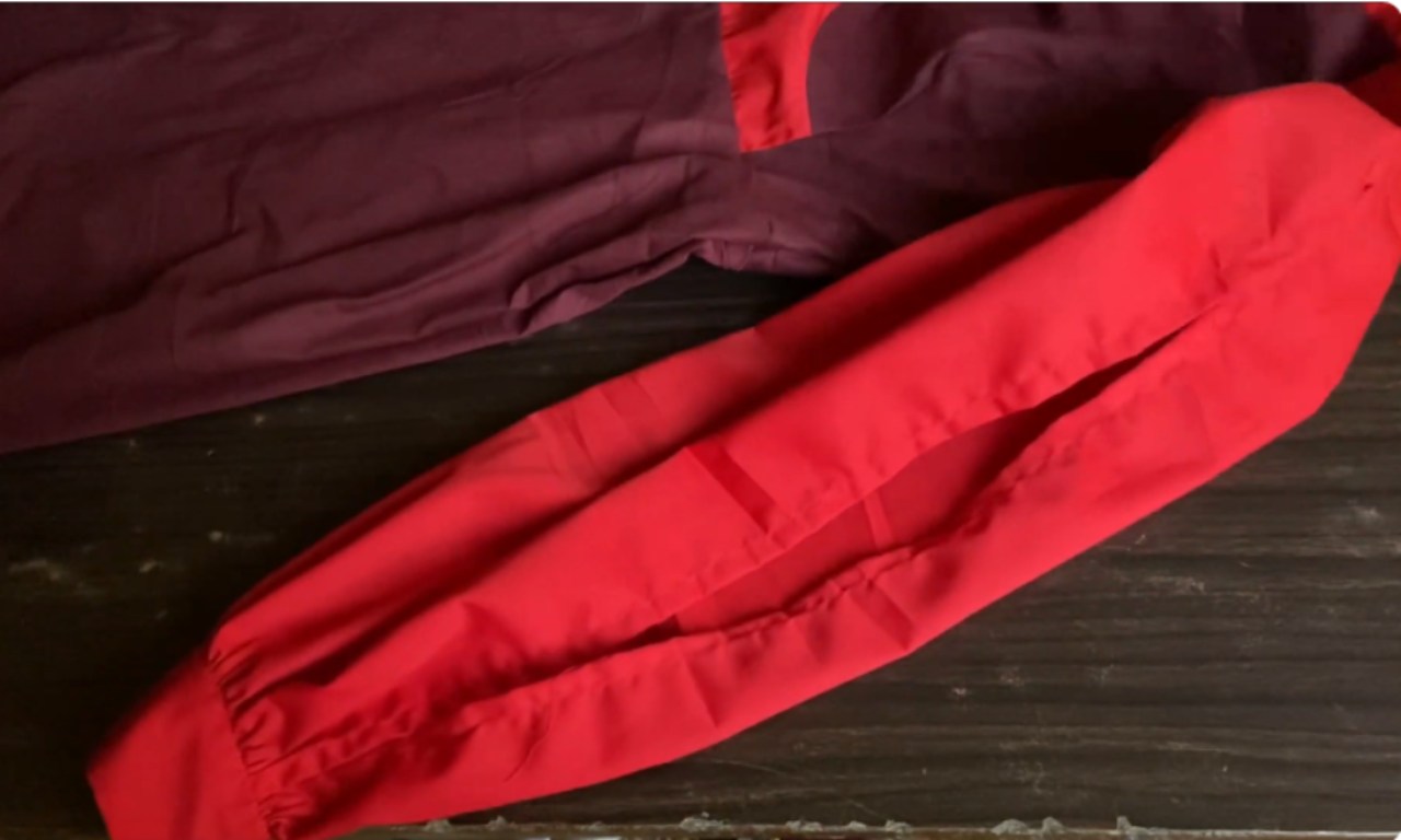 A red and maroon garment showing a completed split sleeve design. The red sleeve has a visible slit running along its length, illustrating the "split" style. The fabric is laid flat on a dark wooden surface.