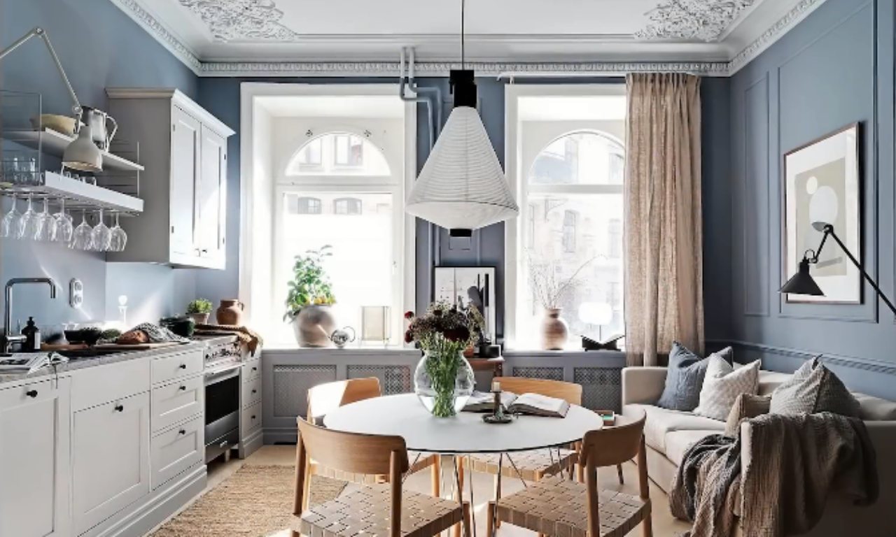 A bright, open-plan living space with light blue walls, a round white dining table, and a neutral sofa arranged to maximize flow