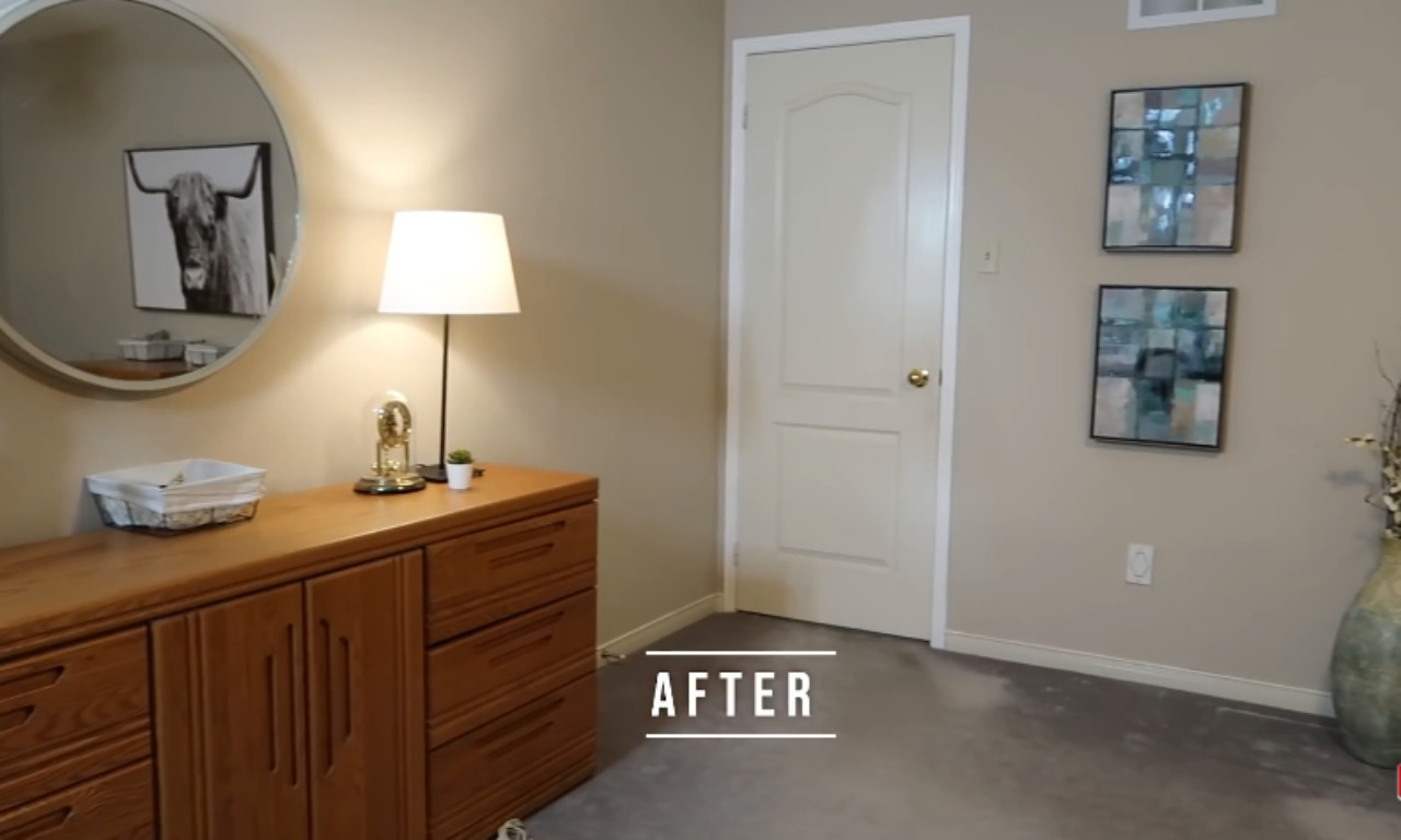 A bedroom view featuring a long, wooden dresser with multiple drawers. A large round mirror hangs above it, reflecting a framed cow print. On the dresser sits a table lamp, and two square abstract wall art pieces are hung vertically on the adjacent wall next to a white door.
