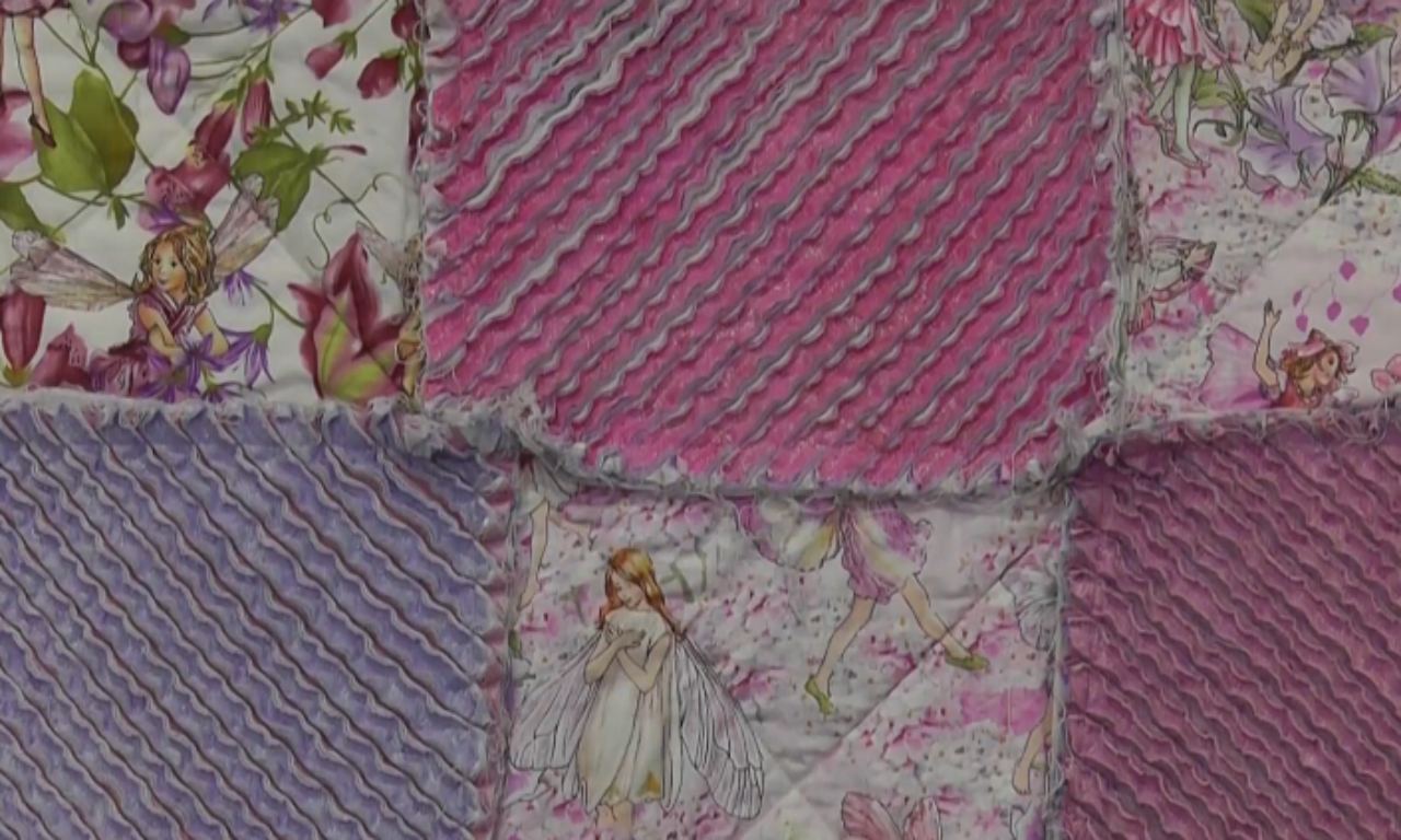 The finished texture of a chenille quilt, showing alternating blocks of fluffy purple and pink chenille next to smooth quilt blocks with a fairy print.