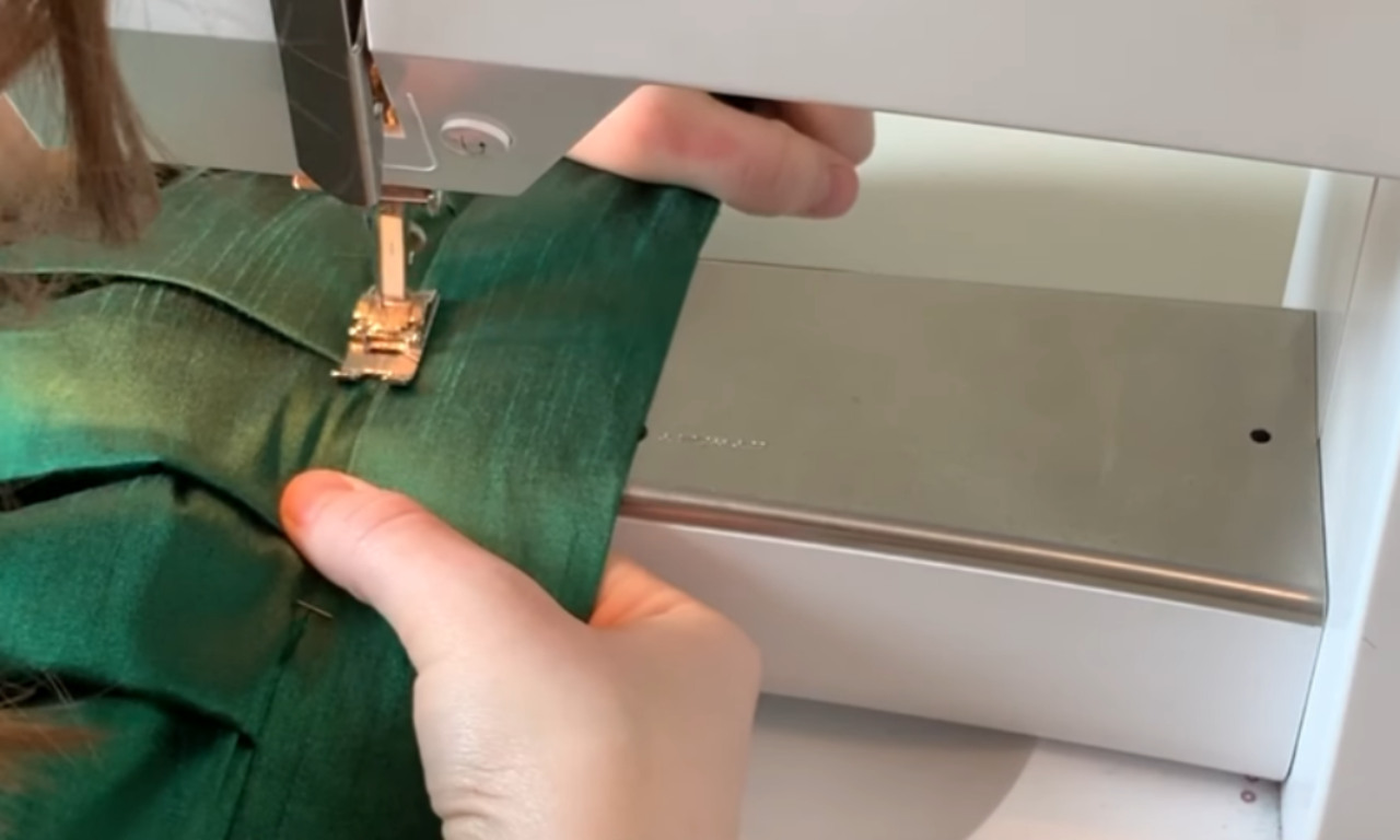 Close-up of a person's hands carefully sewing a green skirt waistband using the stitch-in-the-ditch technique on a sewing machine.