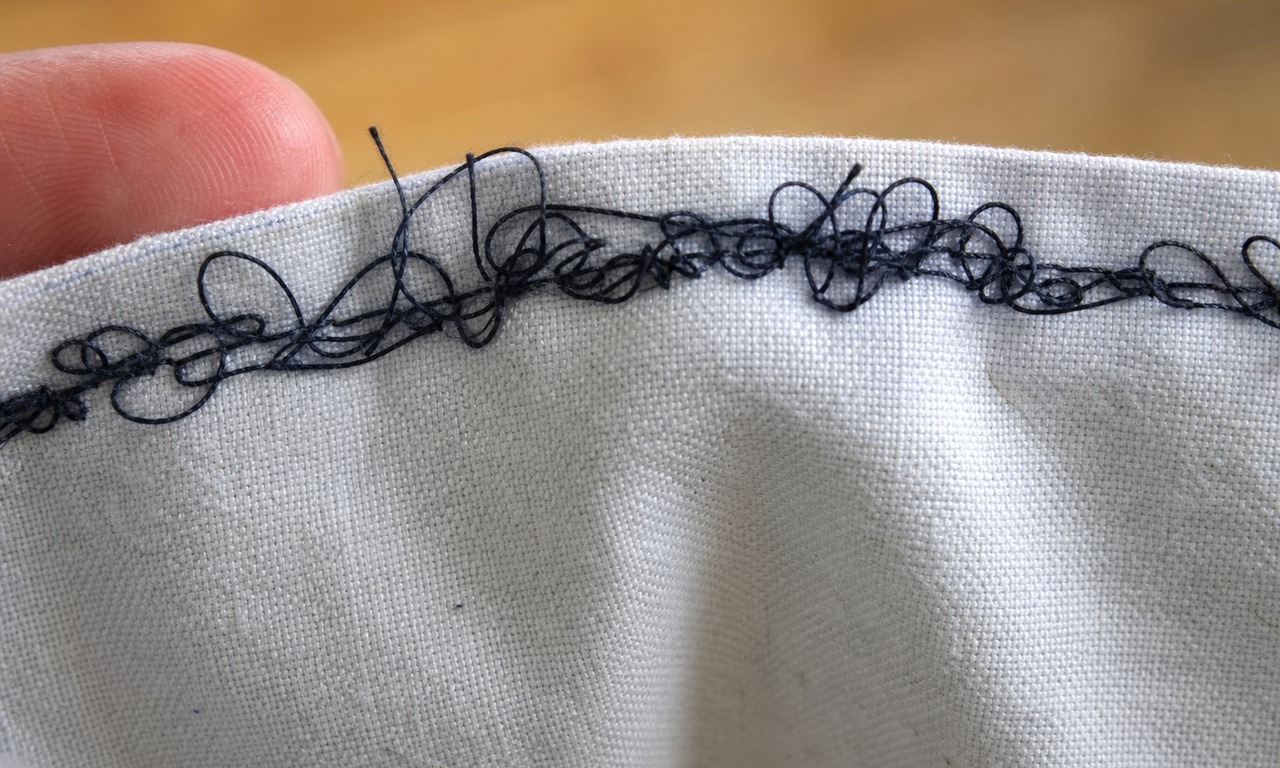 Close-up of dense tangled thread loops on the underside of a cotton seam, seen from below with the fabric folded back