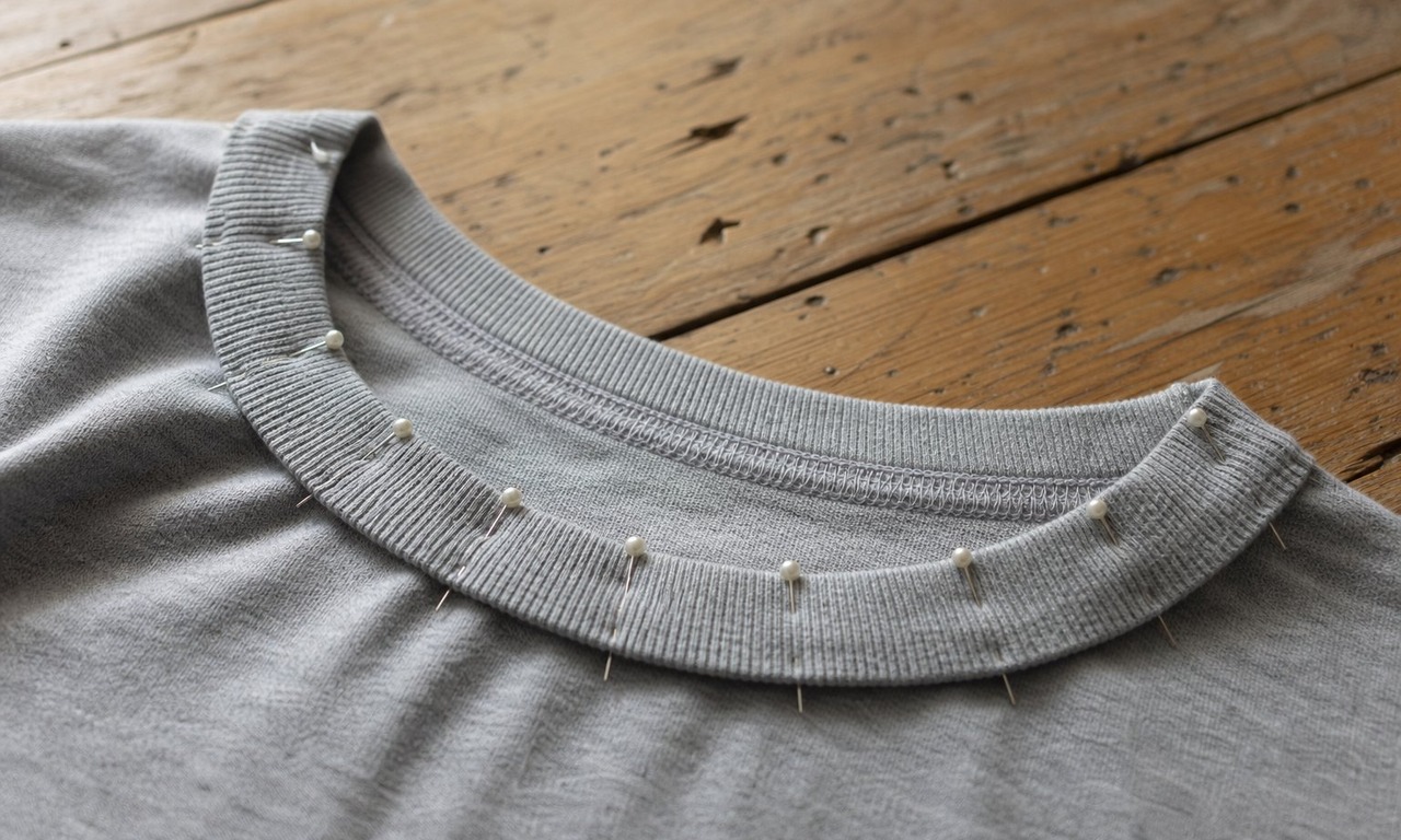 A rib knit neckband pinned to the neck opening of a grey t-shirt with pins spaced evenly around the curve
