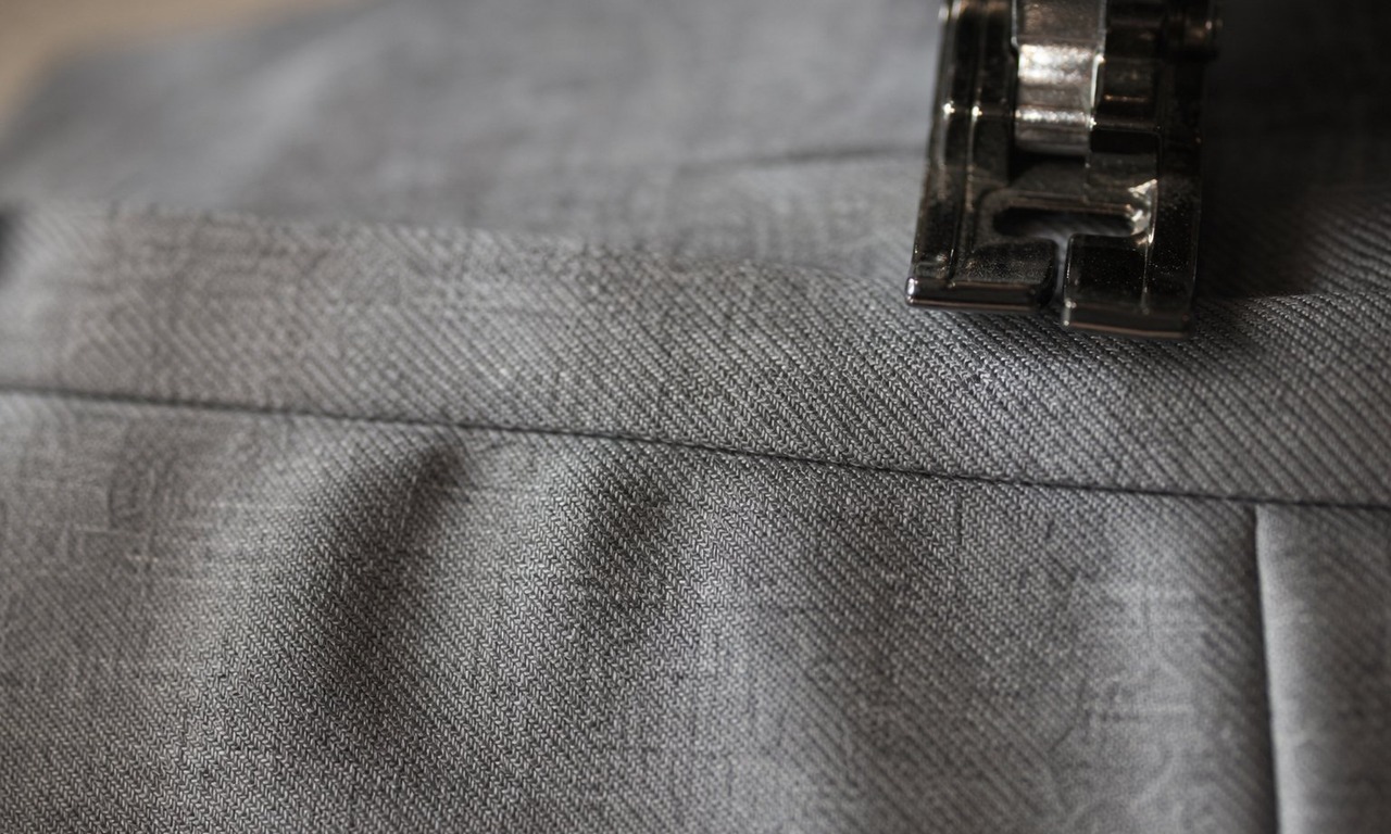 The reattached waistband of grey trousers with stitch-in-the-ditch running in the crease where band meets body